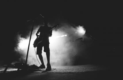 man holding guitar at microphone with fog mist in background