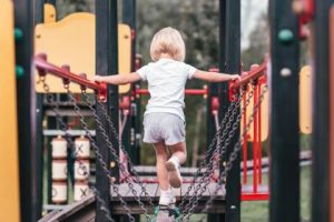 girl on playground walking across beam held up by chains